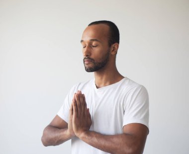 Genç afro adam zihnine konsantre oluyor, ellerini namaste jesti yapıyor, meditasyon yapıyor, yoga nefes egzersizi tekniği stresi azaltıyor. Yaşam tarzı kavramı.