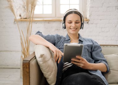 Dijital tablet kullanan, oturma odasındaki kanepesinde dinlenirken film izleyen güzel bir genç kadın. Yaşam tarzı kavramı.