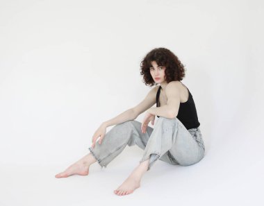 Genç, kıvırcık, güzel bir kadın yerde oturuyor.