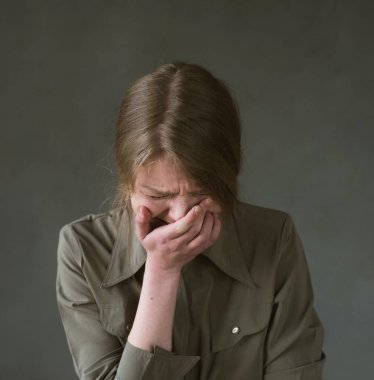 Ağlayan ve acı çeken bir kadın, elini gri bir arka planda tutarak yüzünü kapatıyor..