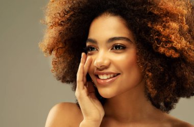Bej arka planda, şehvetli, kıvırcık Afrikalı bir kadının portresi. Güzellik, insanlar ve moda konsepti.