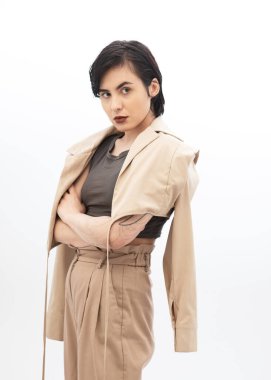 Kısa saçlı, bej ceketli, beyaz arka planda poz veren şık bir genç kadın..