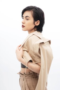 Kısa saçlı, bej ceketli, beyaz arka planda poz veren şık bir genç kadın..