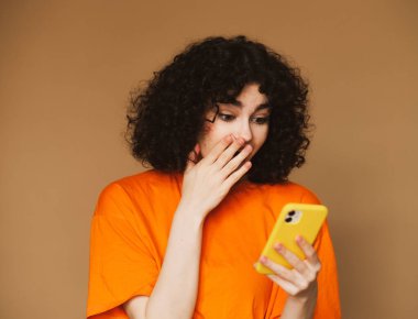 Neşeli, genç, kıvırcık bir kadının cep telefonuyla sohbet edişinin fotoğrafı..