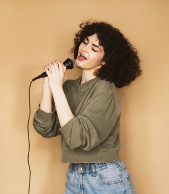 Neşeli, kıvırcık saçlı genç bir kadın mikrofona şarkı söylüyor ve dans ediyor..