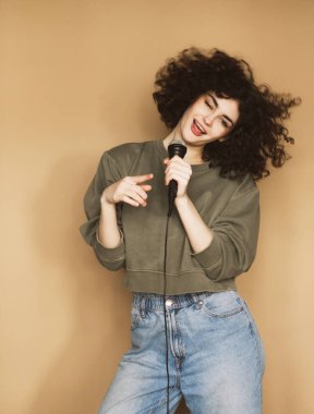 Neşeli, kıvırcık saçlı genç bir kadın mikrofona şarkı söylüyor ve dans ediyor..