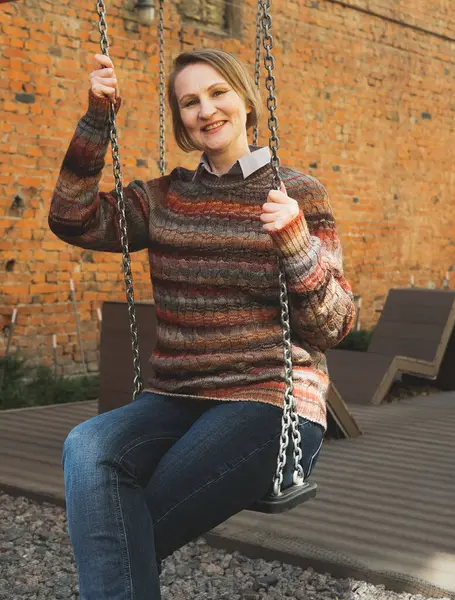 Yaşlı bir kadın yazın şehirde salıncakta sallanıyor..