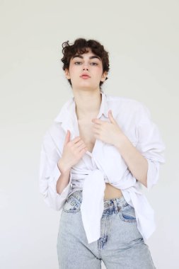 Beyaz arka planda poz veren kot pantolonlu ve beyaz gömlekli güzel bir kadın..