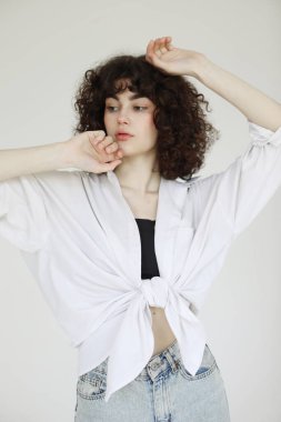 Beyaz arka planda poz veren kot pantolonlu ve beyaz gömlekli güzel bir kadın..