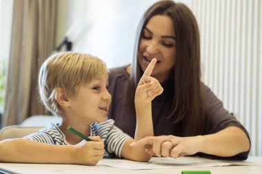 Anne oğluna resim yapmayı öğretiyor. Genç bir kadın ve altı yaşındaki bir çocuk masada oturarak yaratıcı işler yapıyorlar. Yaşam tarzı kavramı.