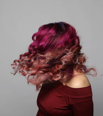 Çok renkli kıvırcık saçlı, saçlarını sallayan, saçlarında rüzgar olan genç bir kadın. Gri arkaplandaki portre. Kapat..