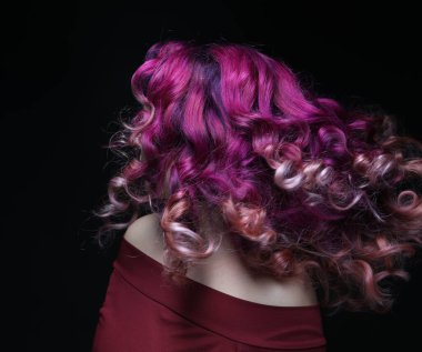 Çok renkli kıvırcık saçlı, saçlarını sallayan, saçlarında rüzgar olan genç bir kadın. Siyah arkaplanda portre.