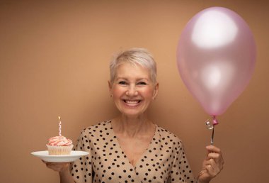 Elinde mum ve elinde balonlarla güzel, gülümseyen yaşlı bir kadın. Bej arkaplan üzerinde portre.