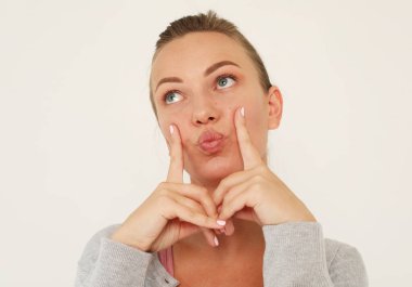 Neşeli, komik, genç bir kadın kameraya yüzünü buruşturur, parmaklarını yanaklarına bastırır, eğlenir. Yaşam tarzı ve duygu konsepti.