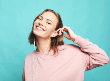 Yaşam tarzı, duygu ve insan konsepti: kulaklıklı, gülümseyen ve dans eden güzel genç kadın, mavi arka planda mutlu hissediyor..