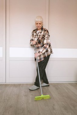Kısa saçlı yaşlı bir kadın odayı paspasla süpürüyor. Yaşam tarzı ve insan kavramı.