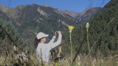 Bir turist kadın çimlerin üzerinde oturuyor ve cep telefonlarıyla fotoğraf çekiyor. Pireneler Dağı..
