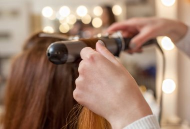 Kuaför, kuaförde uzun kızıl saçlı kuaför kız yapar. Saç maşasıyla bukleler oluşturun. Profesyonel saç bakımı..