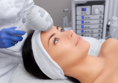 Doktor-kozmetik uzmanı, güzellik salonundaki güzel, genç bir kadının yüz derisinin dondurulması prosedürünü uyguluyor. Kozmetoloji ve profesyonel cilt bakımı..