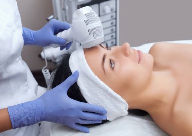 The doctor-cosmetologist makes the procedure Cryotherapy of the facial skin of a beautiful, young woman in a beauty salon.Cosmetology and professional skin care. clipart