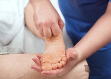 Doktor-ayak hastalıkları uzmanı klinikte hastanın ayağına muayene ve masaj yapar..