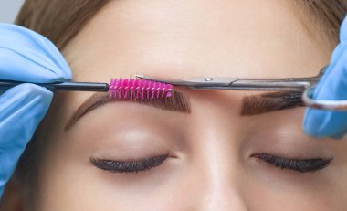 Makyöz kaşlarını makasla kesiyor. Güzel, uzun kirpikleri ve bakımlı kaşları olan bir kız..