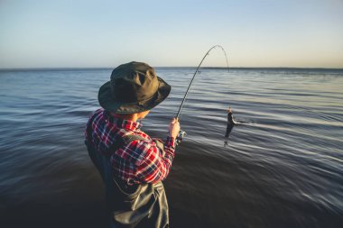 A fisherman with a fishing rod in his hand and a fish caught stands in the water clipart