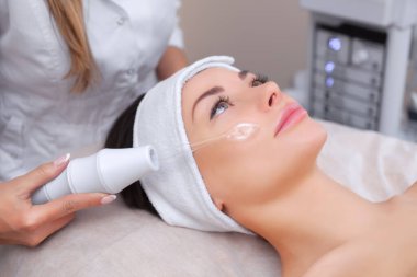 Doktor-kozmetik uzmanı, güzellik salonundaki güzel, genç bir kadının saçı üzerinde mikro-akım terapi uyguluyor. Kozmetik ve profesyonel cilt bakımı..