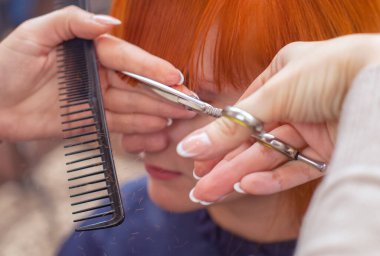 Kuaför Kızıl saçlı kız bir güzellik salonu ile genç bir saç makasla saçını yapar.