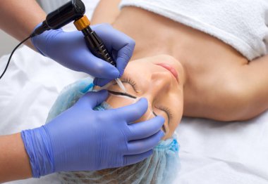 Güzellik salonunda kalın kaşları olan güzel bir kadının kalıcı makyajı. Yakından bir güzellik uzmanı kaş dövmesi yapıyor..