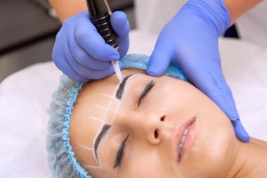 Güzellik salonunda kalın kaşları olan güzel bir kadının kalıcı makyajı. Yakından bir güzellik uzmanı kaş dövmesi yapıyor..