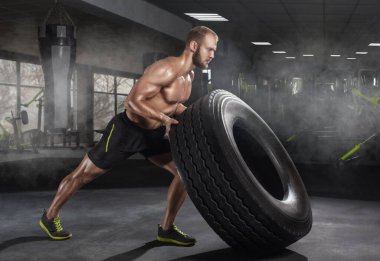 Genç yetişkin bir adam spor salonunda lastik takla atıyor. Spor konsepti, yağ yakma ve sağlıklı bir yaşam tarzı..