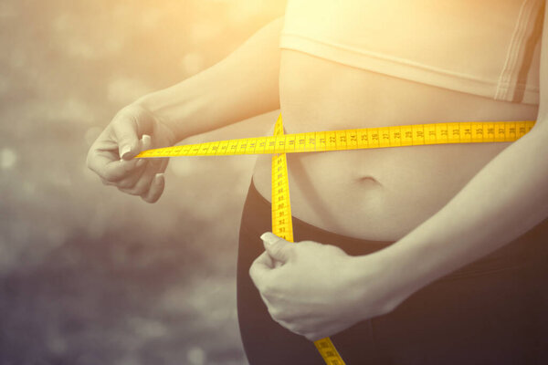 Спортивная девушка, измеряющая талию желтой измерительной лентой. Снижение избыточного веса. Здоровый образ жизни
.