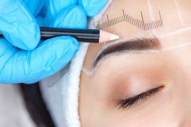 Güzellik salonunda kalın kaşları olan güzel bir kadının kalıcı makyajı. Yakından bir güzellik uzmanı kaş dövmesi yapıyor..