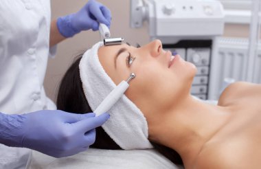 Kozmetik uzmanı bu aleti güzellik salonundaki genç ve güzel bir kadının mikro-akım terapisi için bir prosedür haline getiriyor. Kozmetoloji ve profesyonel cilt bakımı.