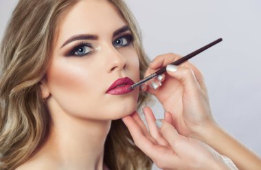 The make-up artist paints the lips of a beautiful woman,  completes the day's make-up in the beauty salon. Professional skin care.
