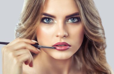 The make-up artist paints the lips of a beautiful woman,  completes the day's make-up in the beauty salon. Professional skin care.
