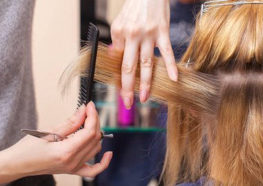 Kuaför bir saç makasıyla genç bir kıza, bir sarışına kuaförde saç kestirir..