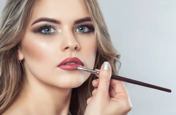 The make-up artist paints the lips of a beautiful woman,  completes the day\'s make-up in the beauty salon. Professional skin care.