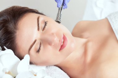 Kozmetik uzmanı, güzellik salonundaki güzel, genç bir kadının yüz derisinin mikro cilt bakımını yapıyor. Kozmetoloji ve profesyonel cilt bakımı..