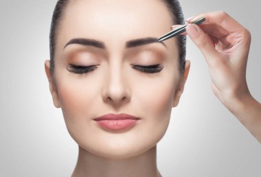 Makyöz, kınayla lekelenmeden önce bir kadına cımbızla kaş yoluyor..