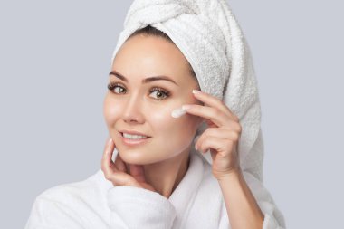 Güzel bir genç kadının portresi, bir duştan sonra yüzüne krem sürer. Yüz ve vücut bakımı.