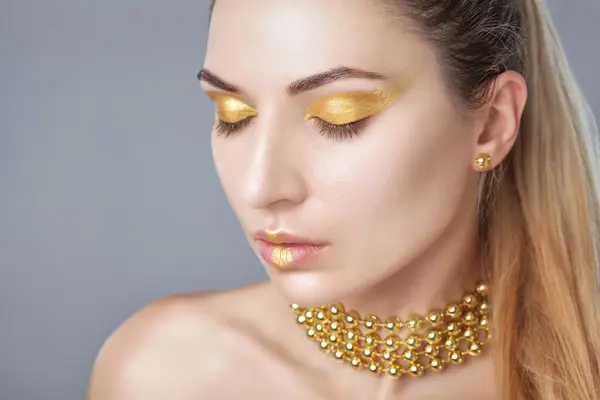 Portrait of a beautiful happy woman with beautiful creative makeup in gold colors. She has gold beads on her neck, in her hands and gold earrings. Make-up concept.