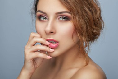 Güzel kızıl saçlı, kıvırcık saçlı, taze makyajlı, kalın kaşlı ve güzellik salonunda temiz tenli bir kadının portresi. Yüzü yakın plan. Gri arkaplanda makyaj konsepti.