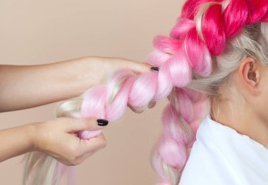 Kuaför, pembe kanekalonlarla örgü örüyor. Güzel sarışın güzellik salonu. Güzel saç stilleri..