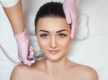 Kozmetik uzmanı, güzellik salonundaki güzel bir kadının yüzünün mikro cilt bakımını yapıyor. Kozmetoloji ve profesyonel cilt bakımı..