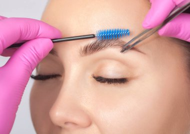 Makyöz, kınayla lekelenmeden önce bir kadına cımbızla kaş yoluyor..