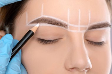 Permanent make-up for eyebrows of beautiful woman with thick brows in beauty salon. Closeup beautician doing tattooing eyebrow. Professional makeup and cosmetology skin care.