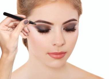 Makyöz, dumanlı göz makyajlı bir kadına cımbızla kaş yoluyor. Güzel kalın kaşlar yakın çekim. Profesyonel makyaj ve kozmetoloji cilt bakımı.