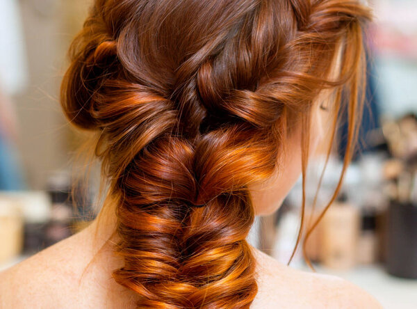 Beautiful woman with long red hair at the beauty salon, hairdresser braided a braid in a beauty salon. Professional hair care and creating hairstyles.